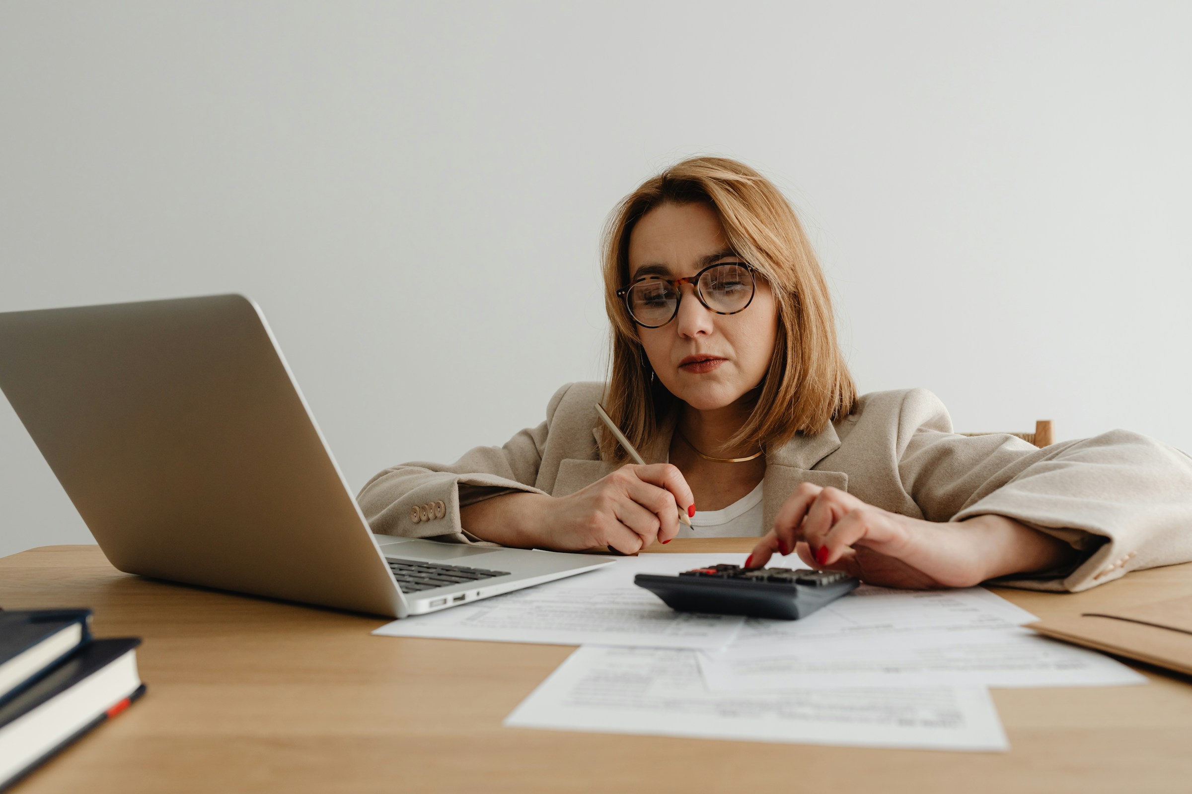 A woman sits at a desk with a laptop and documents, using a calculator, pondering the question: How long do tax returns take?