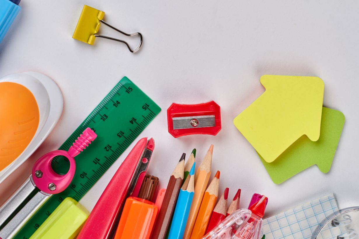 A variety of colorful stationery items, including pencils, a ruler, a binder clip, sticky notes, and a sharpener—all essential for organizing your 2024 tax claims—are arranged on a white surface.