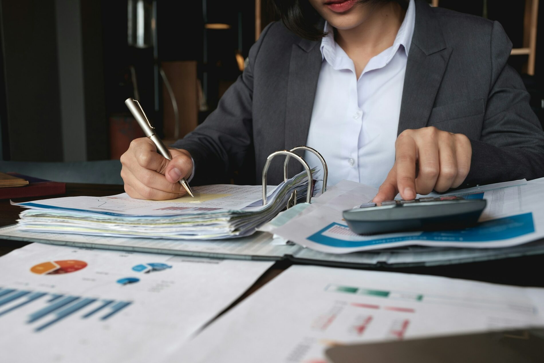 A person in a suit working on financial documents, using a calculator and taking notes with a pen. Charts and graphs are visible on the table, perhaps calculating important figures related to STSL Tax.