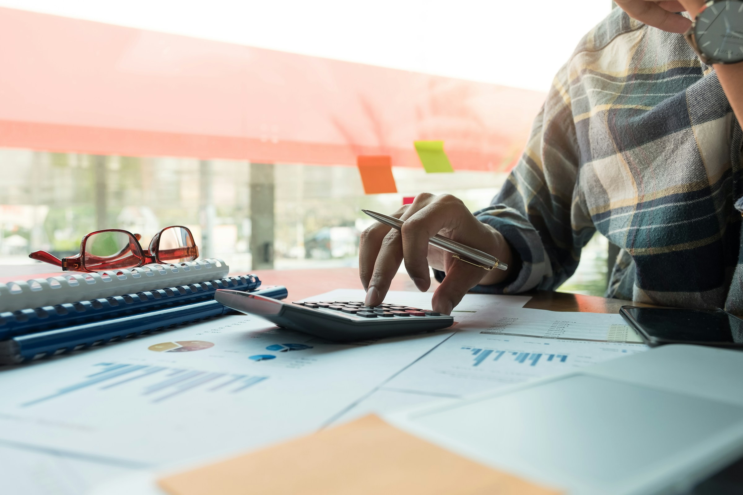 A person using a calculator, surrounded by documents with charts and graphs on a well-lit desk, is researching "What is STSL Tax?" Reading glasses and notebooks are nearby.