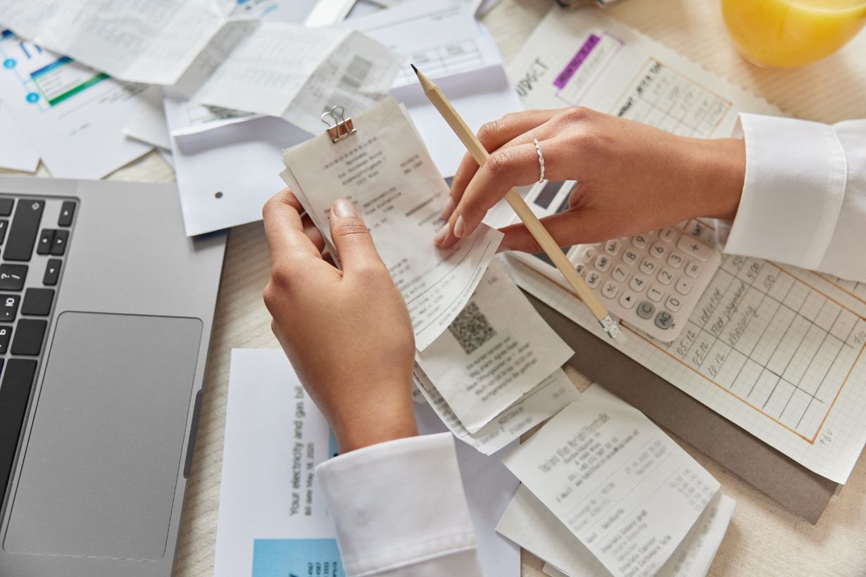 A person is meticulously organizing receipts and documents at a desk adorned with a laptop, notepad, and pencil, diligently ensuring everything aligns with ATO Guidelines for the 2024 tax season.