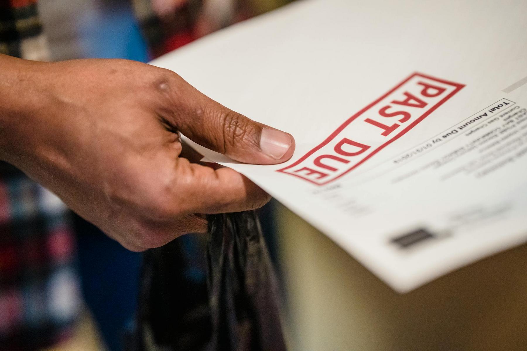 A hand holding an envelope labeled “PAST DUE” in large red letters.