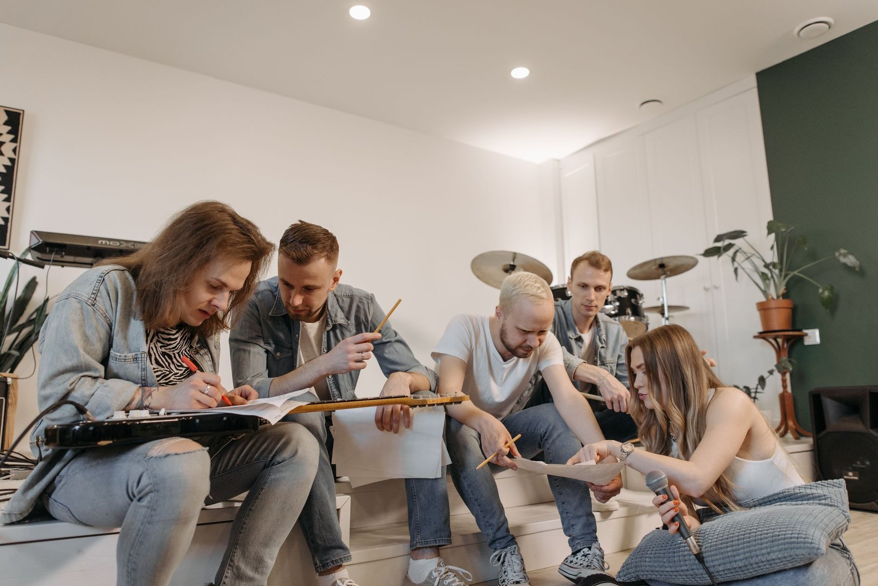 Five band members sitting together in a rehearsal studio, reviewing and writing on paperwork while they work out how the band will run