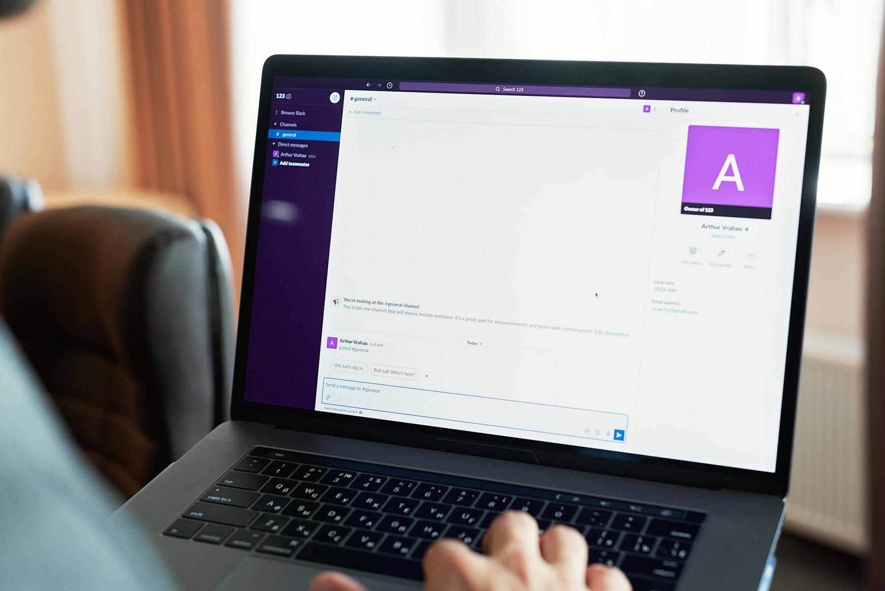 A person using a laptop displaying a Slack workspace with a direct message conversation open on the screen.
