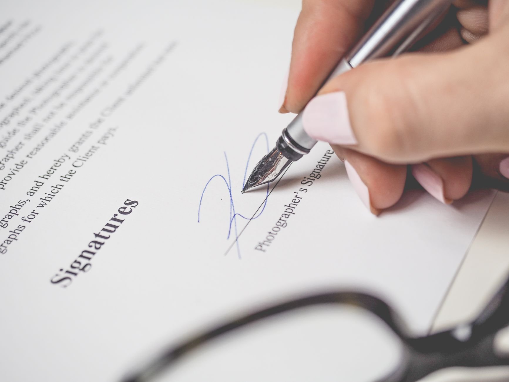 Close-up of a hand signing a photographer's client contract with a fountain pen, setting out deposit and payment terms for creative work