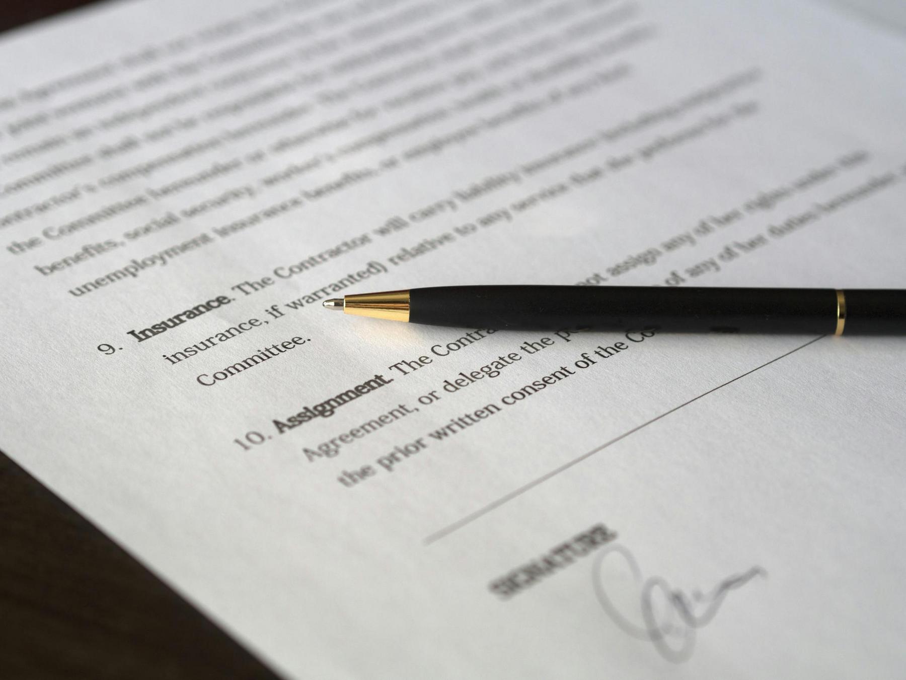 A black and gold pen rests on a document near a signature line and the headings "Insurance" and "Assignment.