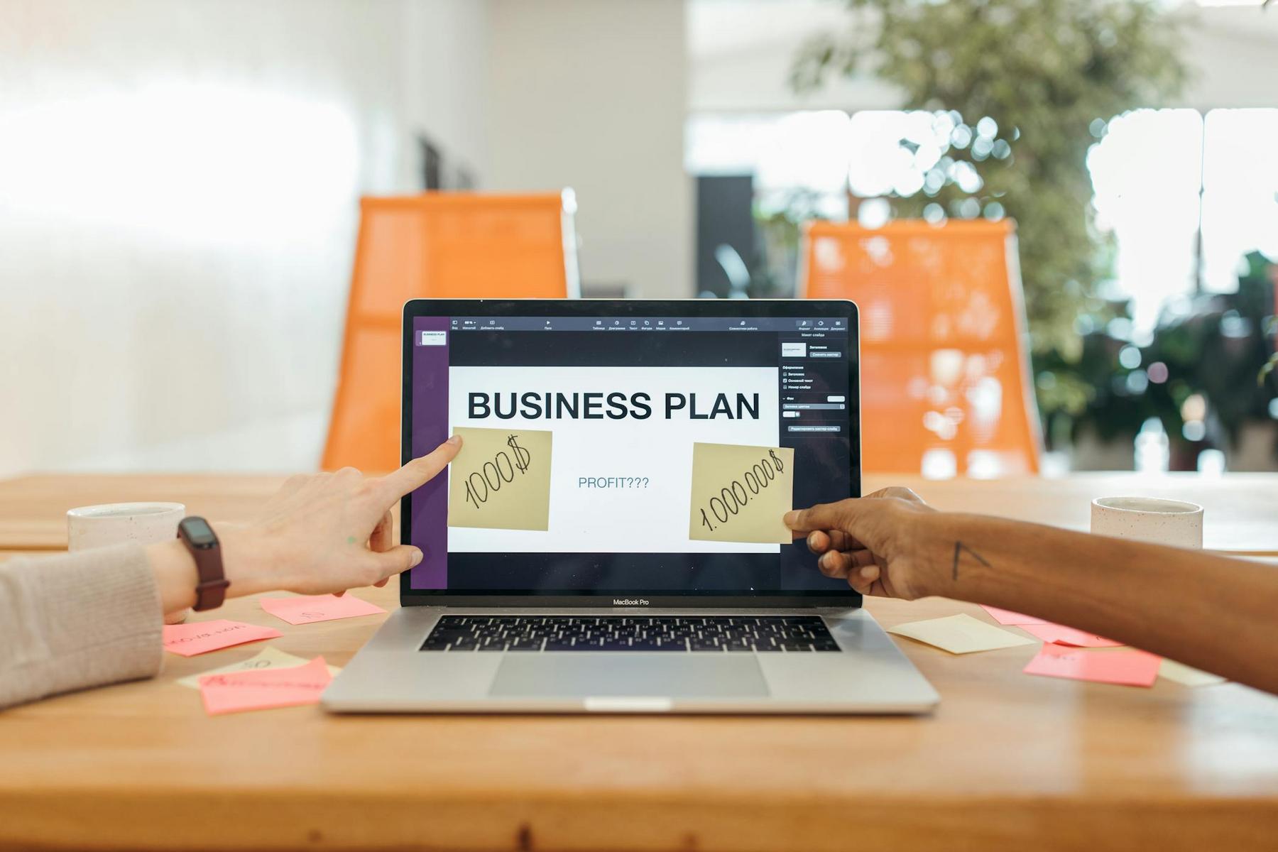 Two people point at a laptop displaying a "BUSINESS PLAN" slide; sticky notes on the screen show "10,000,000" and the question "PROFIT???" is visible.