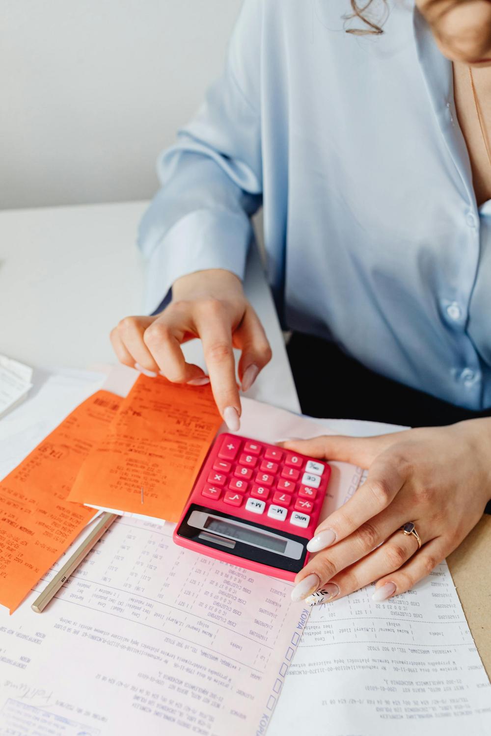 A person uses a pink calculator to review receipts and financial documents at a desk.
