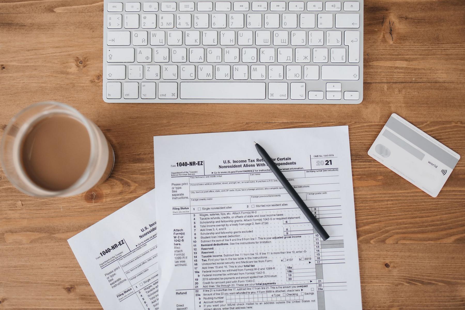 A filled-out 1040 tax form with a pen, credit card, glass of coffee, and a computer keyboard on a wooden desk.