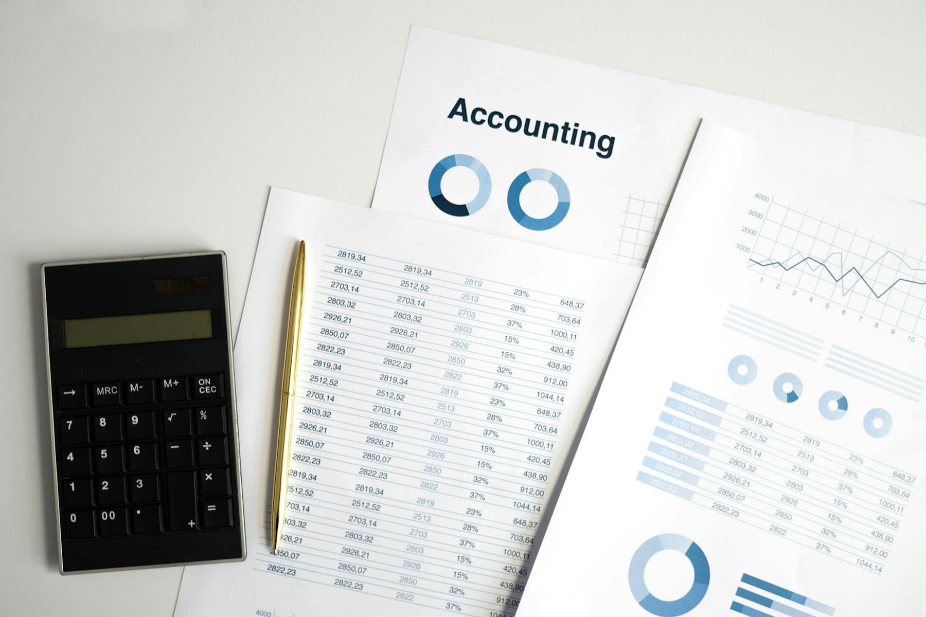 A calculator, a pen, and accounting documents with charts, graphs, and financial data are displayed on a white surface.