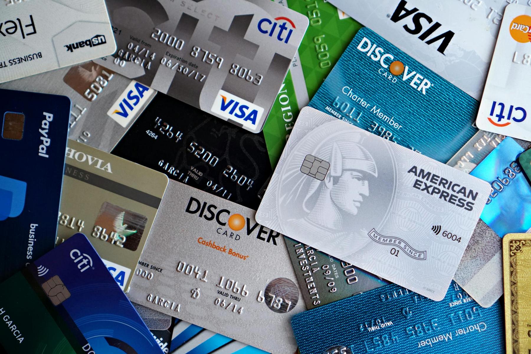 A variety of credit cards from different issuers, including Discover, American Express, Visa, Citi, and PayPal, are spread out in an overlapping arrangement.