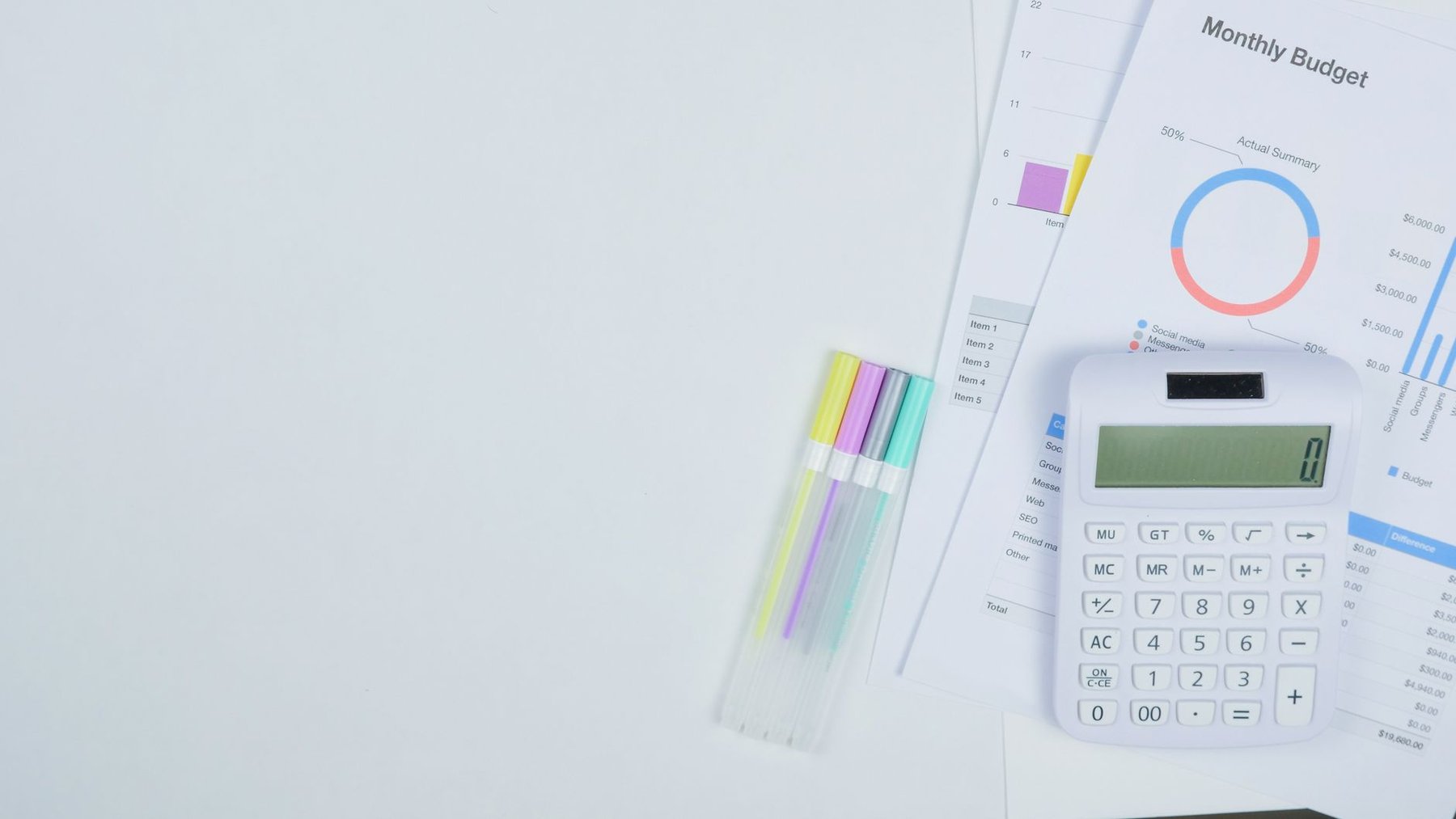 Monthly budget report with charts next to a calculator and pastel highlighters on a clean white desk, ready for a monthly financial check-in