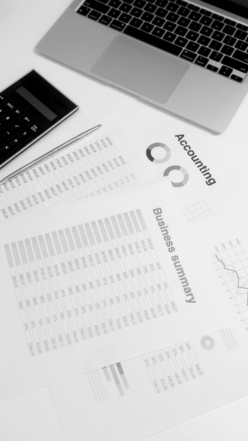 A calculator, pen, and printed financial documents labeled "Business summary" and "Accounting" on a desk next to a laptop.