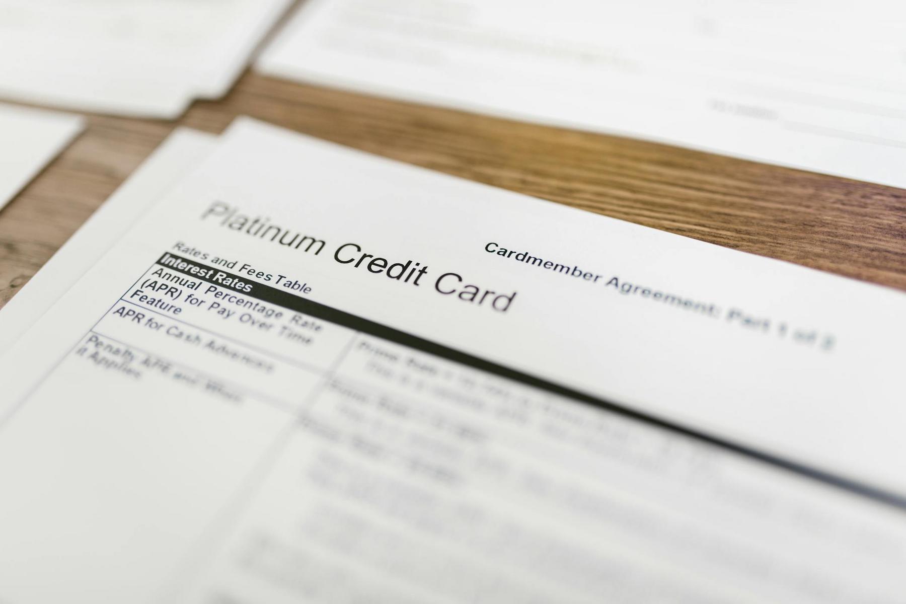 Close-up of a platinum credit card agreement document with information about interest rates and fees visible on a wooden surface.