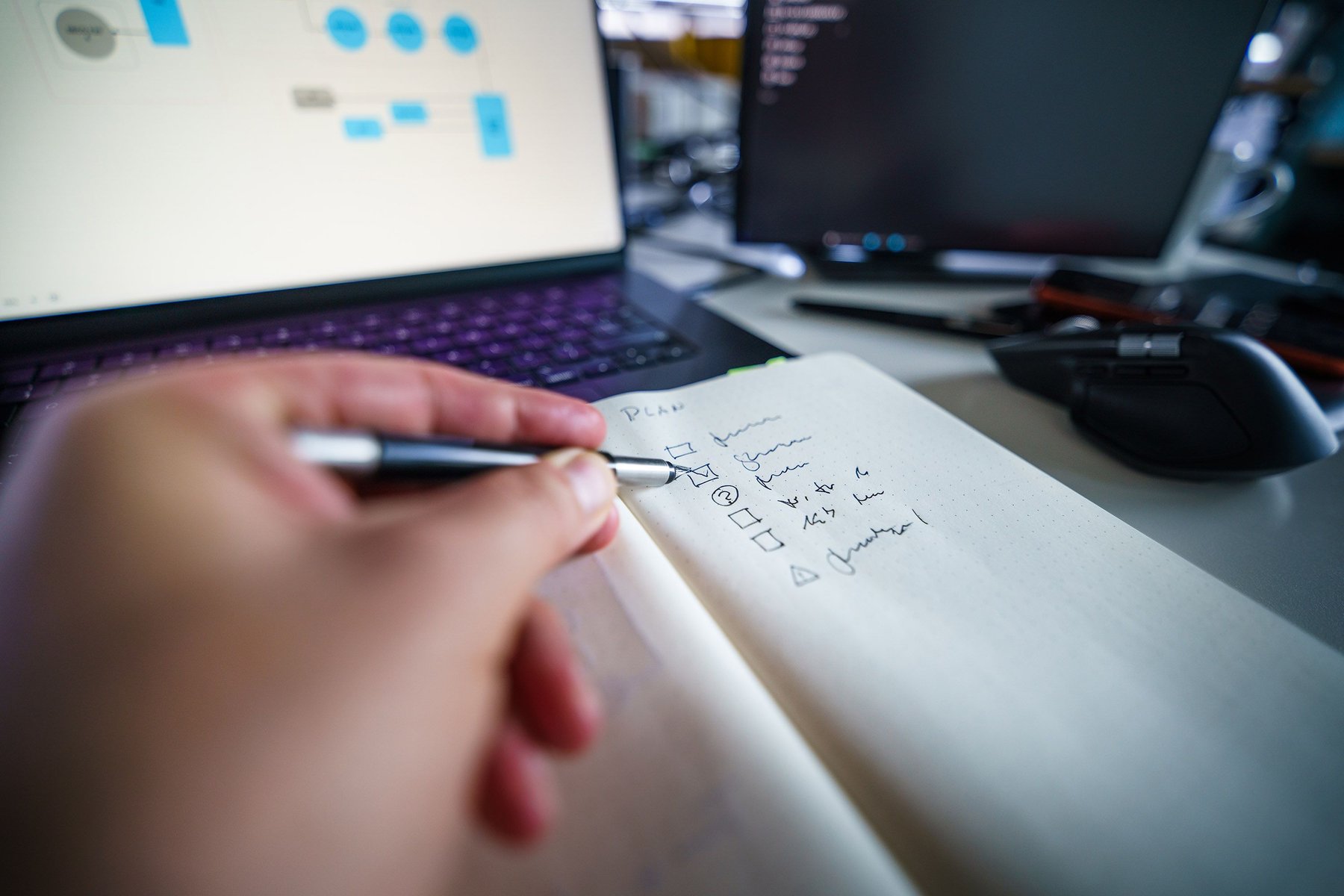 Freelancer ticking off a handwritten checklist in a notebook beside a laptop while planning to start a freelance business