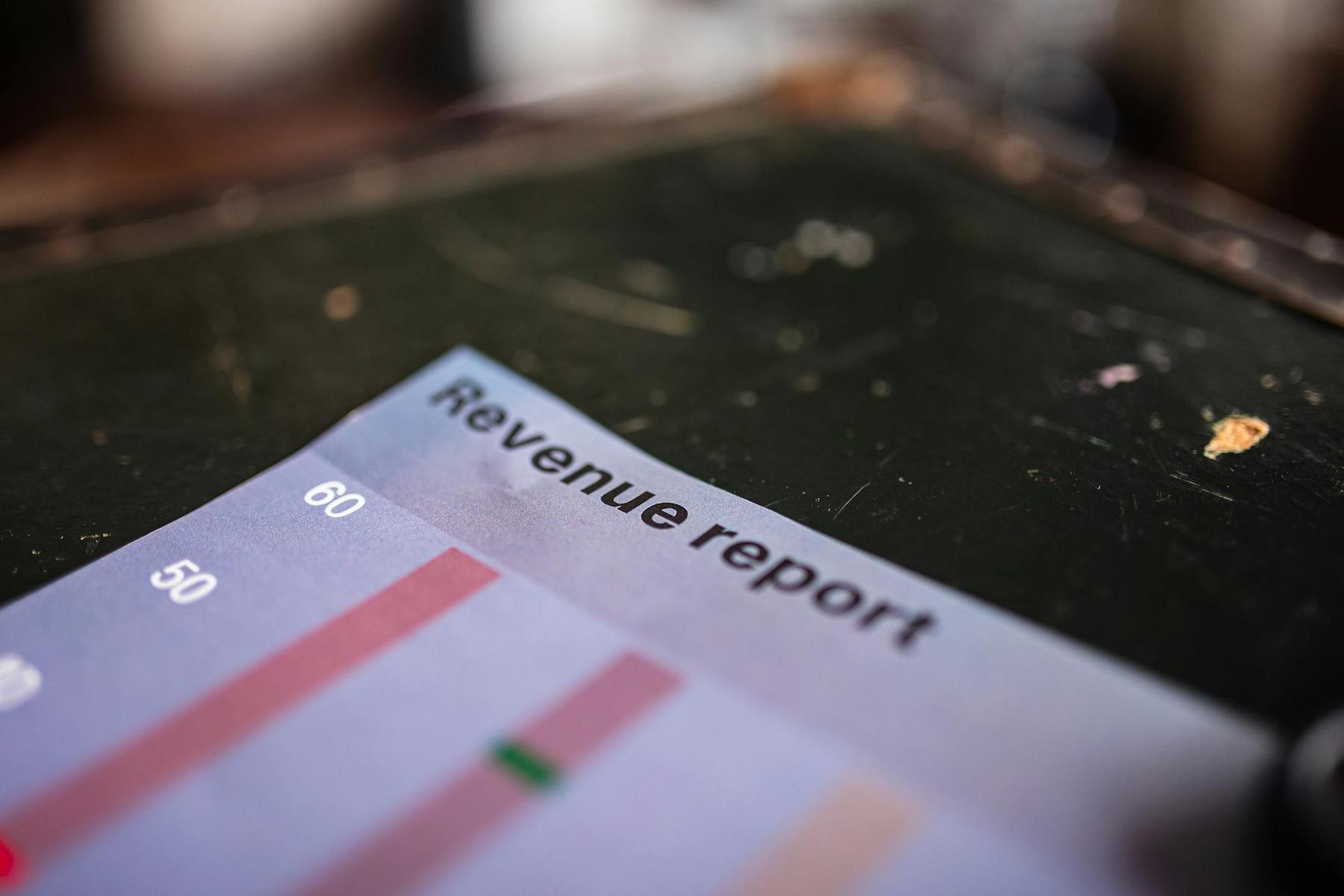 A close-up of a printed revenue report with a bar chart, showing numbers and colored bars, on a dark surface.
