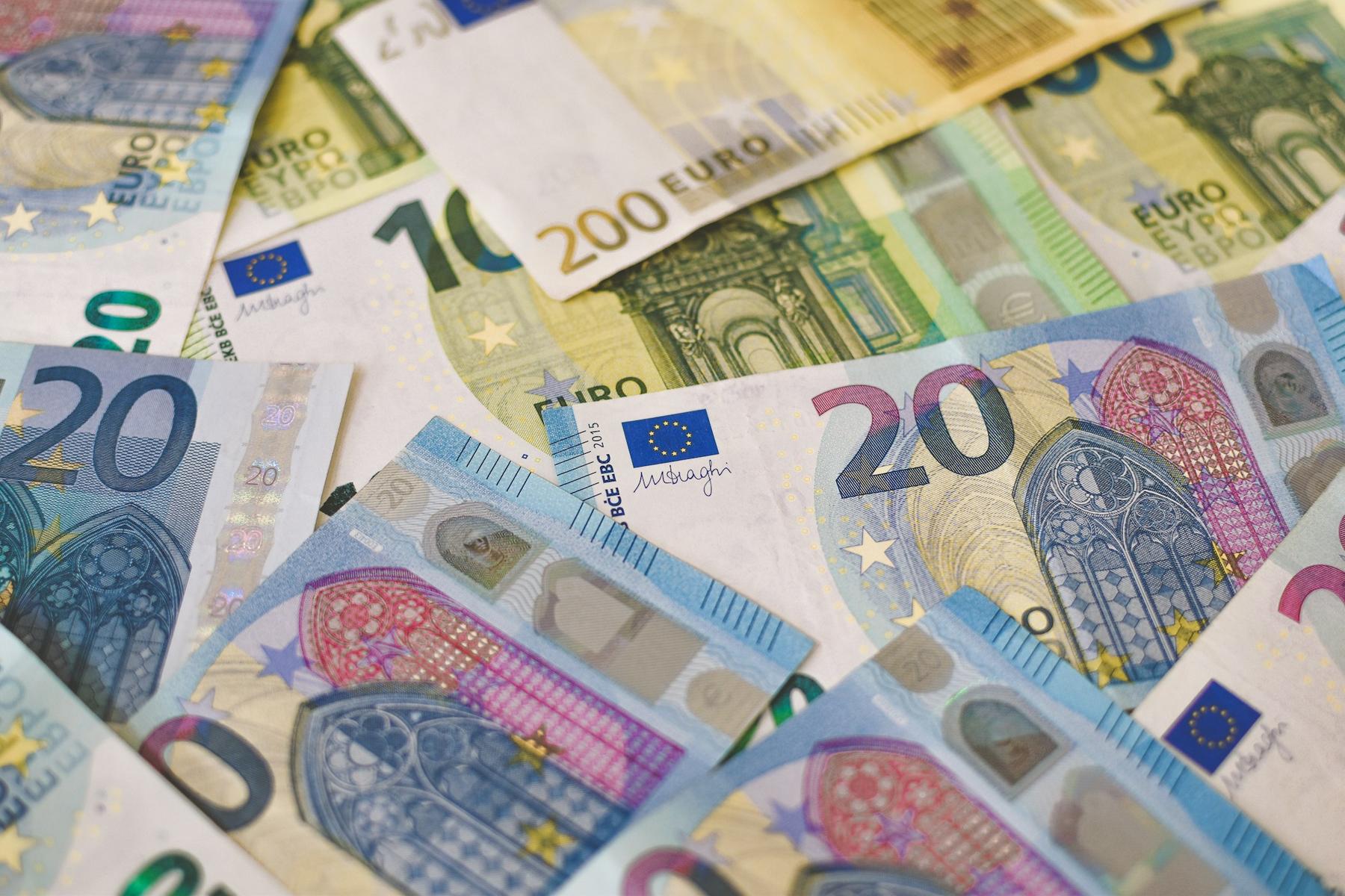 Various denominations of Euro banknotes scattered, including 10, 20, and 200 Euros, featuring architectural designs and security features.